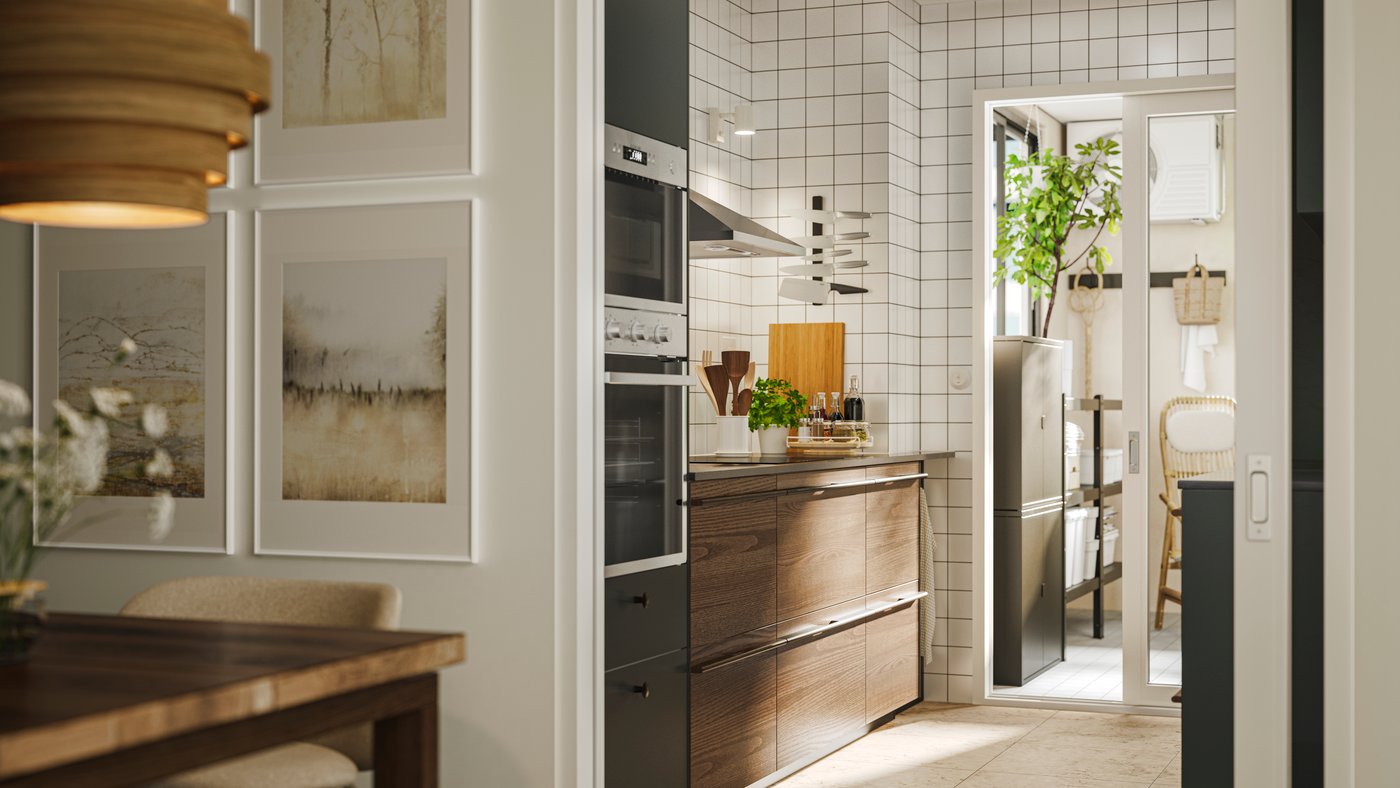 Kitchen with STENSTA dark brown ash veneer fronts, tiled backsplash, and a bright pantry with plants and a wicker chair.