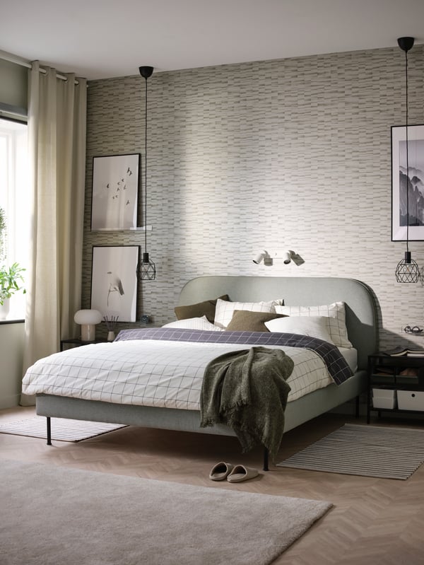 An upholstered bed frame in Gunnared light green, two black pendant lamps and framed art prints.