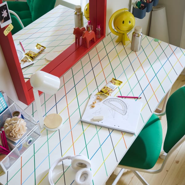 Bureau LAGKAPTEN/SPÄND à motif quadrillé multicolore et chaise de bureau verte, lampe blanche et miroir rouge.