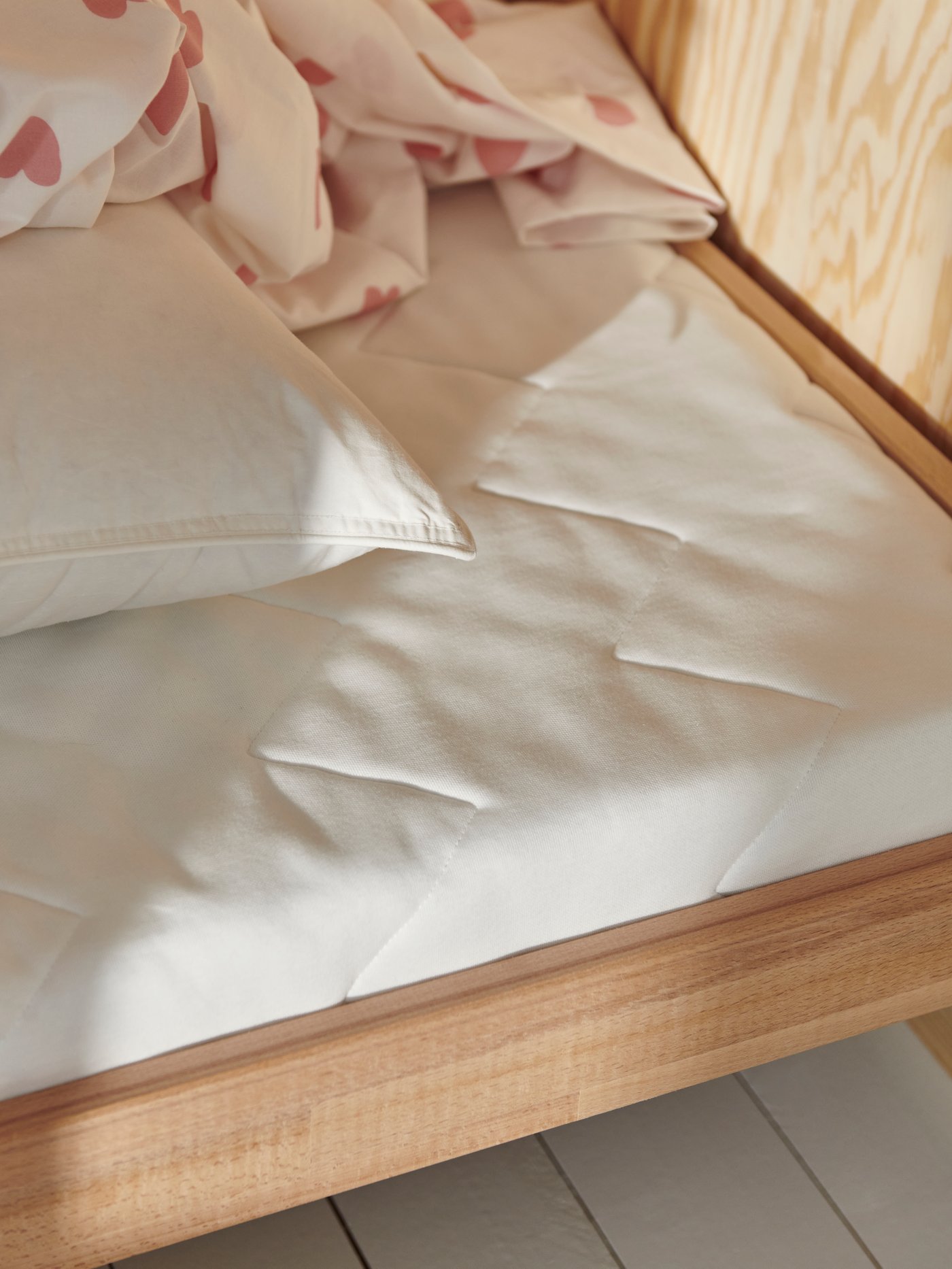 The end of a SNIGLAR bed with guard rail that has an UNDERLIG foam mattress and heart pink/white BARDRÖM bed linen on it.