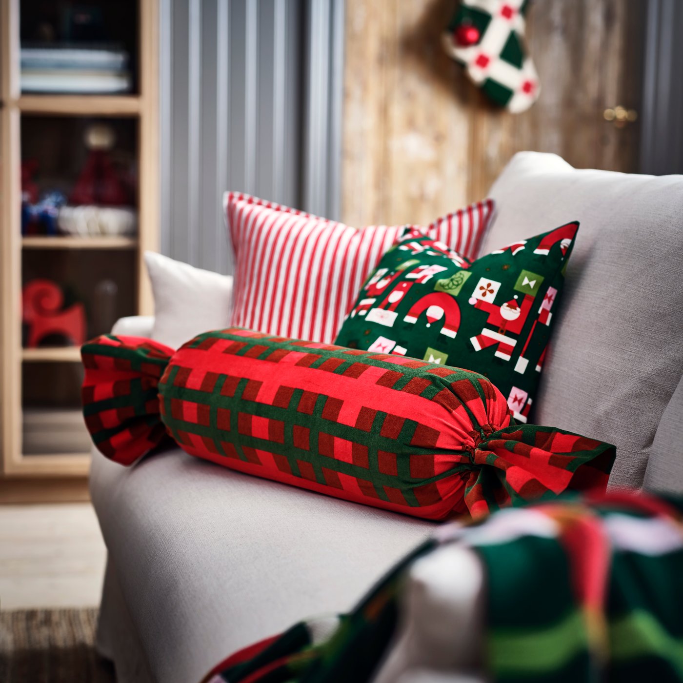 A candy-shaped VINTERFINT cushion with a bold pattern designed by Evelina Kroon is on sofa with other festive cushions.