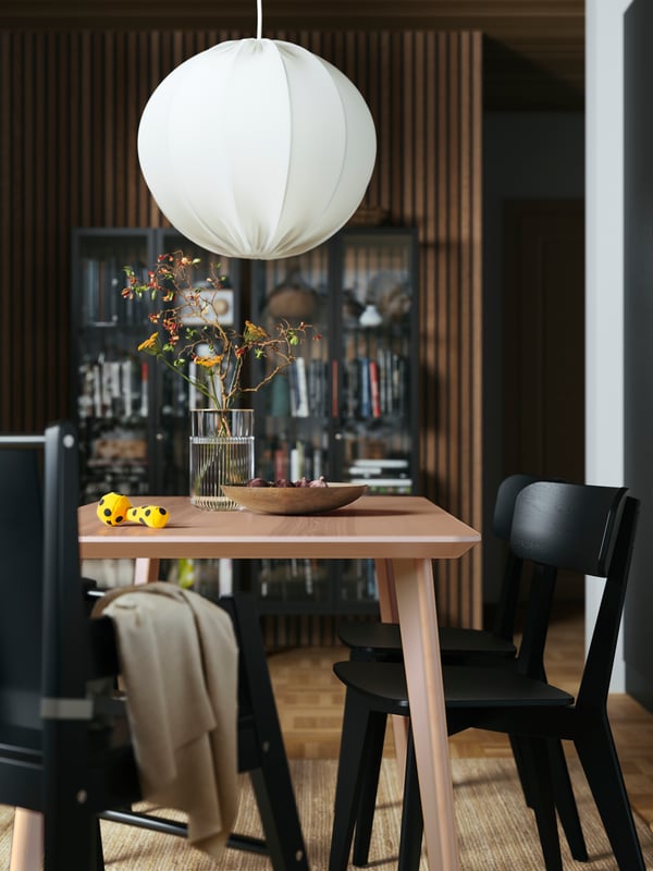 Una habitación con una mesa de comedor LISABO en chapa de roble y sillas LISABO negras, una lámpara de techo REGNSKUR/SUNNEBY en blanco en la parte superior.