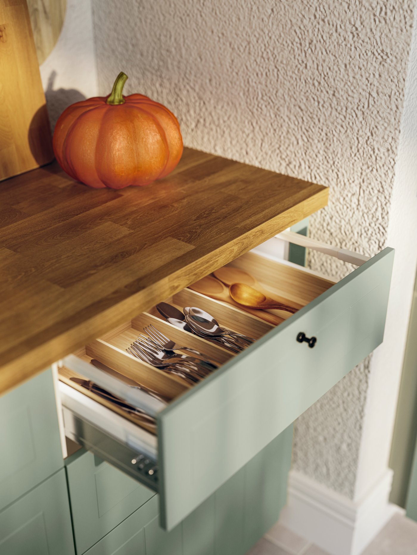 Una cubierta de cocina SÄLJAN en tonos madera instalada sobre muebles de cocina color menta. SObre la cubierta hay un zapallo.