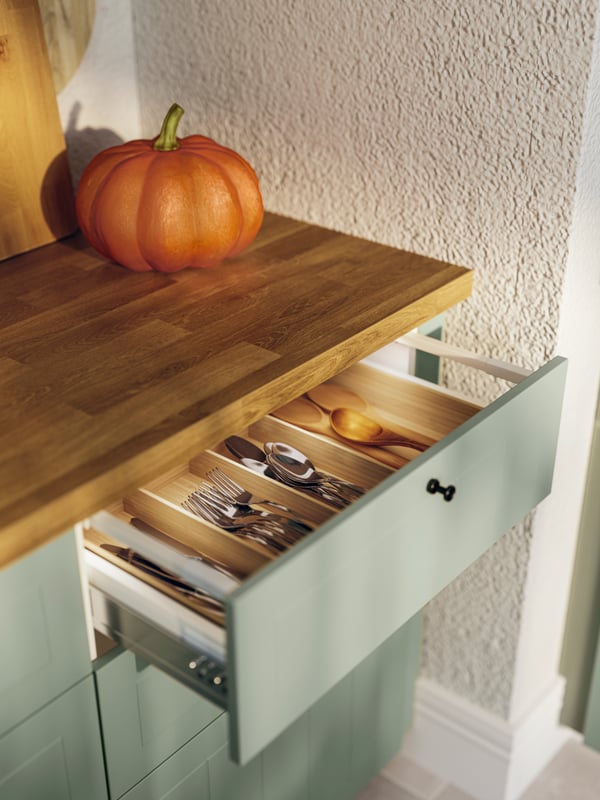 A STENSUND drawer front in light green, drawer open with cutlery, and a pumpkin on a SÄLJAN worktop in oak effect/laminate.