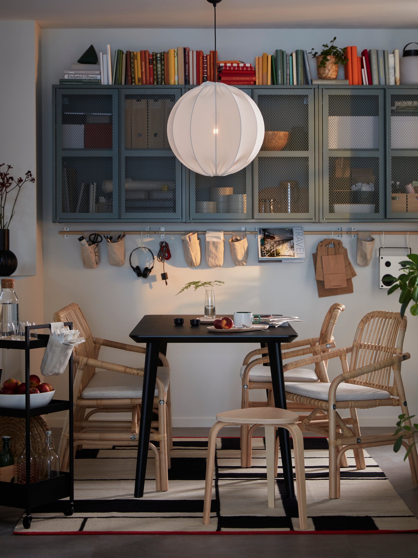A dining area formed by a black LISABO table and SALNÖ rattan chairs and bench. On the wall are grey-green IVAR cabinets.
