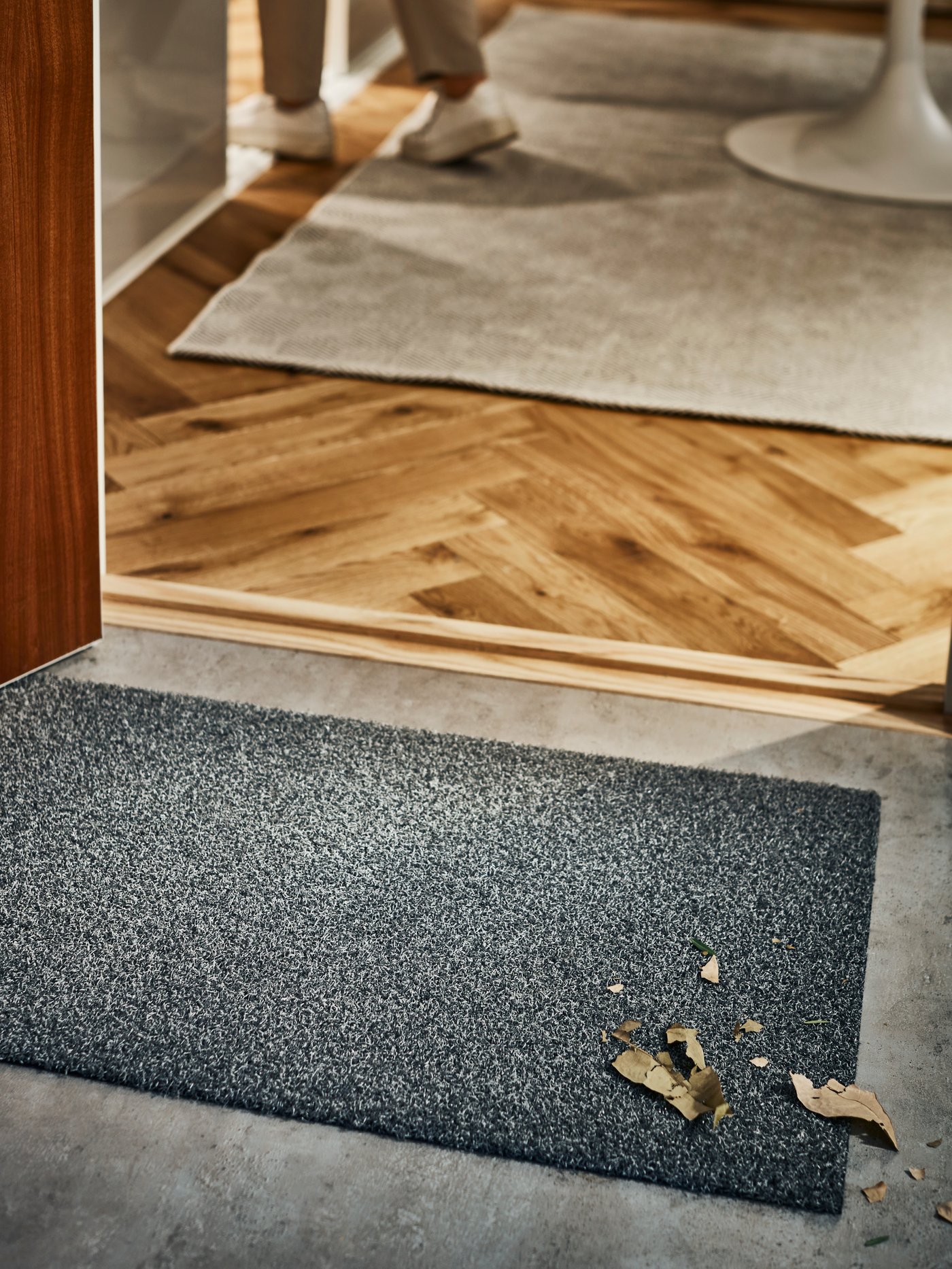 An in/outdoor grey OPLEV door mat sits at the front door of a home that has the front door open.
