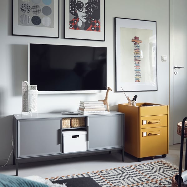 Una sala con mueble para TV TULLSTORP gris y al costado una cajonera amarilla IDÅSEN.