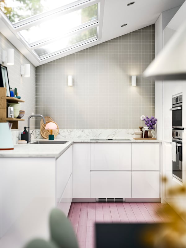 A modern kitchen with sleek VOXTORP white kitchen fronts in a space with a skylight ceiling, and a worktop with marble effect.
