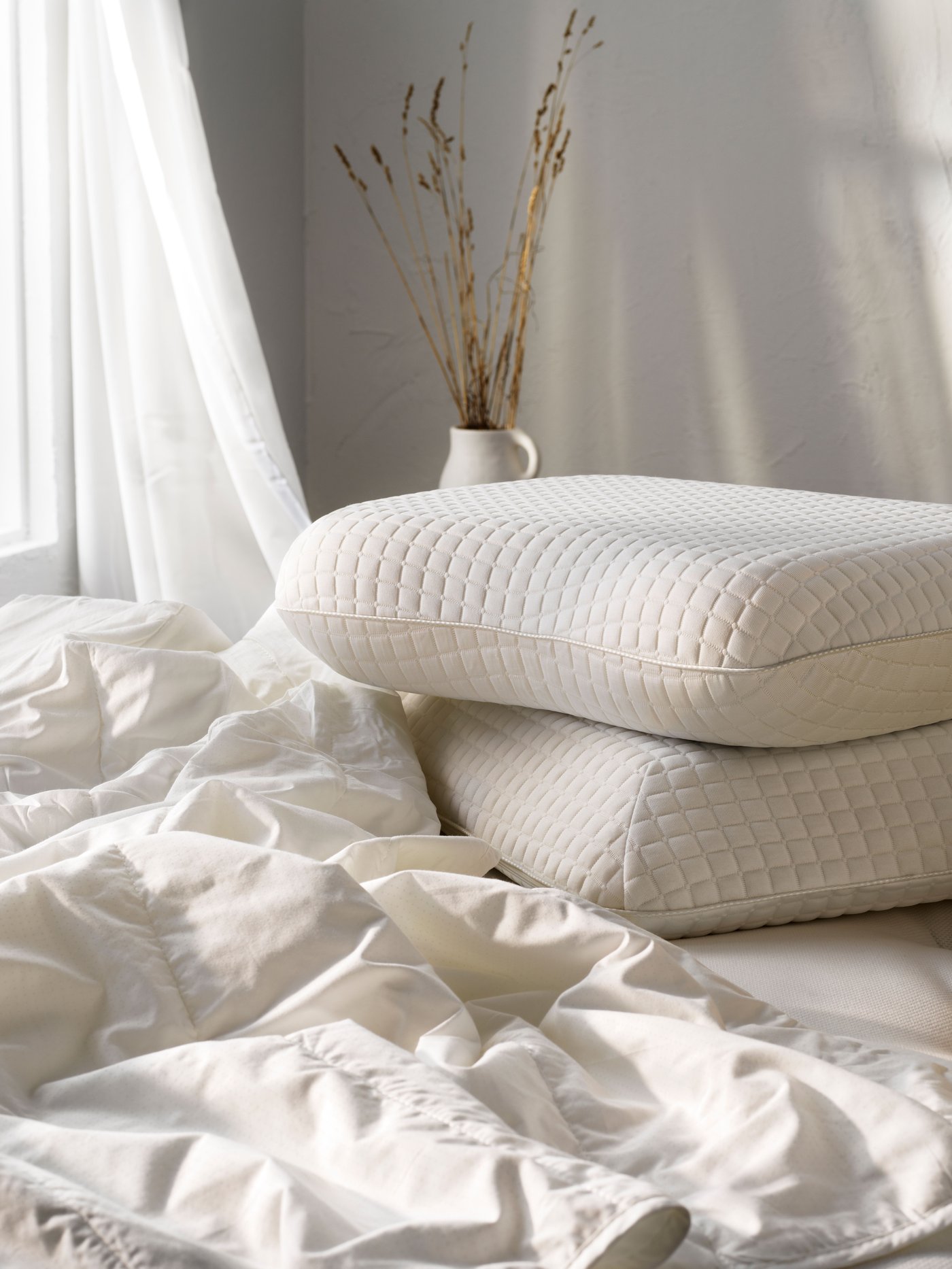 Eine kühle GRUSSTARR Bettdecke liegt gemeinsam mit zwei ergonomischen, kühlenden KLUBBSPORRE Kissen auf einem Bett.