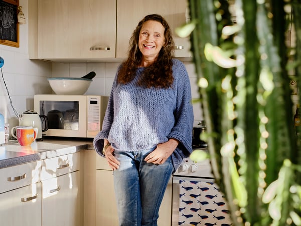 Lady standing in kitchen smiling with her hands in the pocket. 