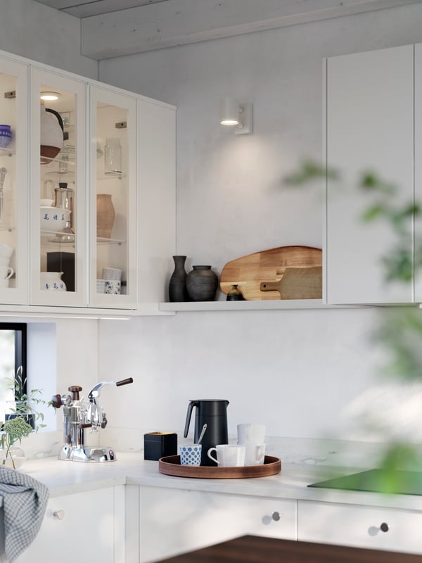 A bright kitchen has white glossy RINGHULT fronts and wall cabinets with HEJSTA glass doors, and a white wall shelf.