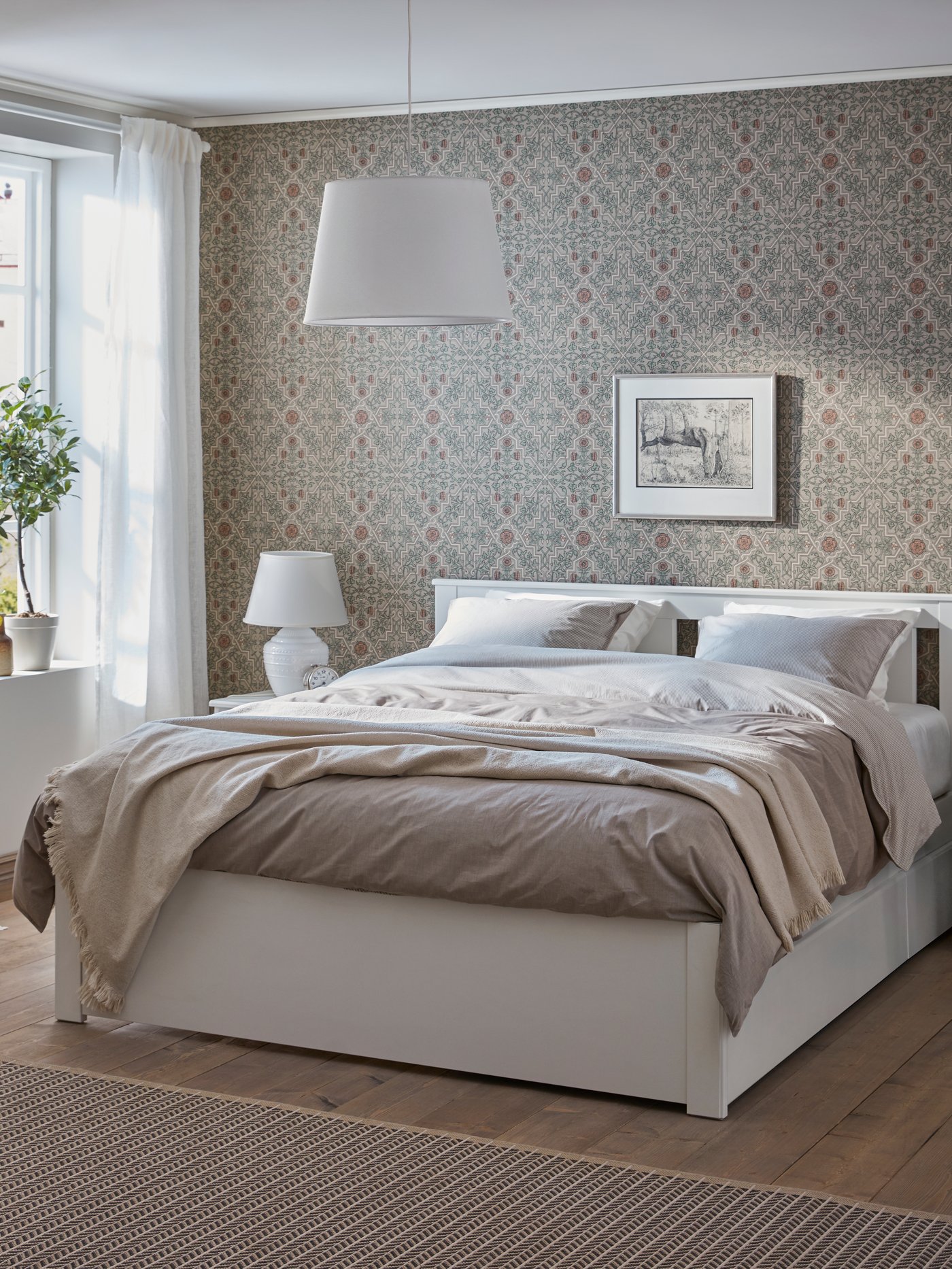 Una cama doble blanca con ropa de cama en tonos rosas y blanco sobre una alfombra IKEA.