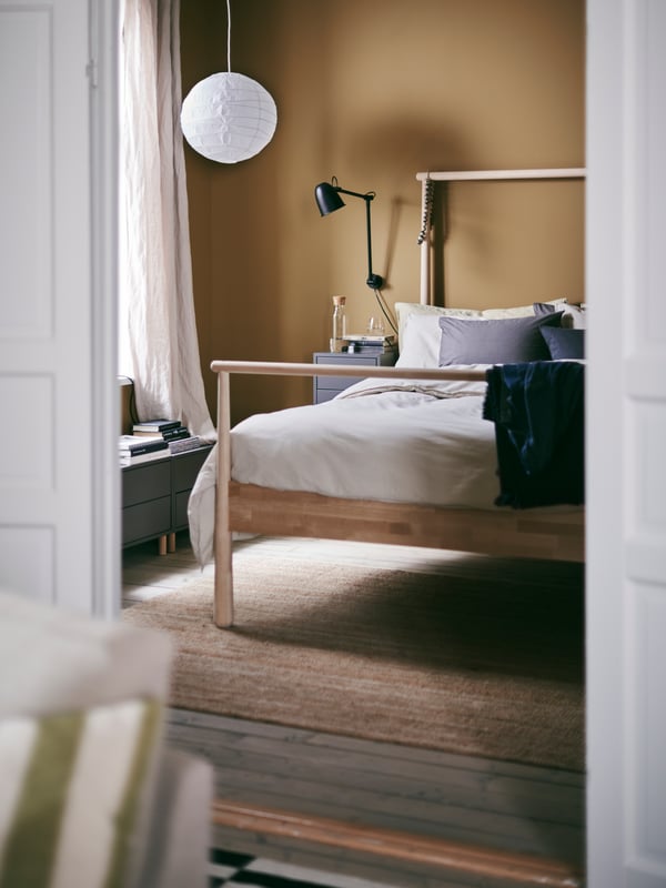 L’aperçu d’une chambre chaleureuse et accueillante avec un lit GJÖRA en bouleau et un abat-jour de suspension REGOLIT en papier.