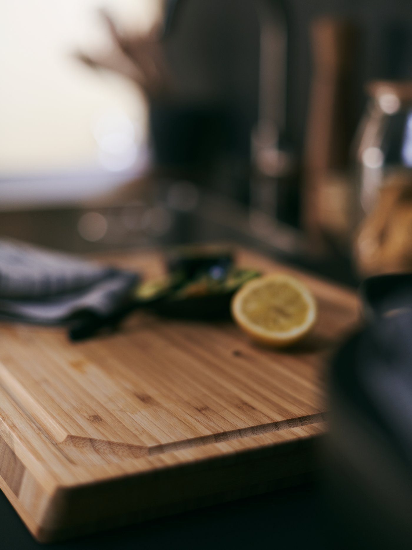 The APTITLIG chopping board made from durable bamboo, with half a cut lemon on it together with a tea towel and other objects.