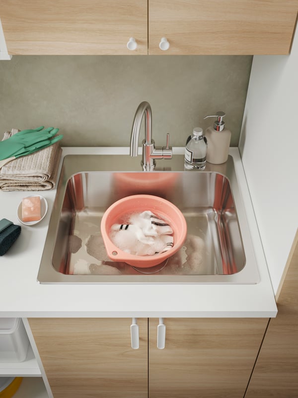 An ENHET laundry solution holding a PEPPRIG wash tub with articles of washing in it, and RINNIG cleaning gloves in green.