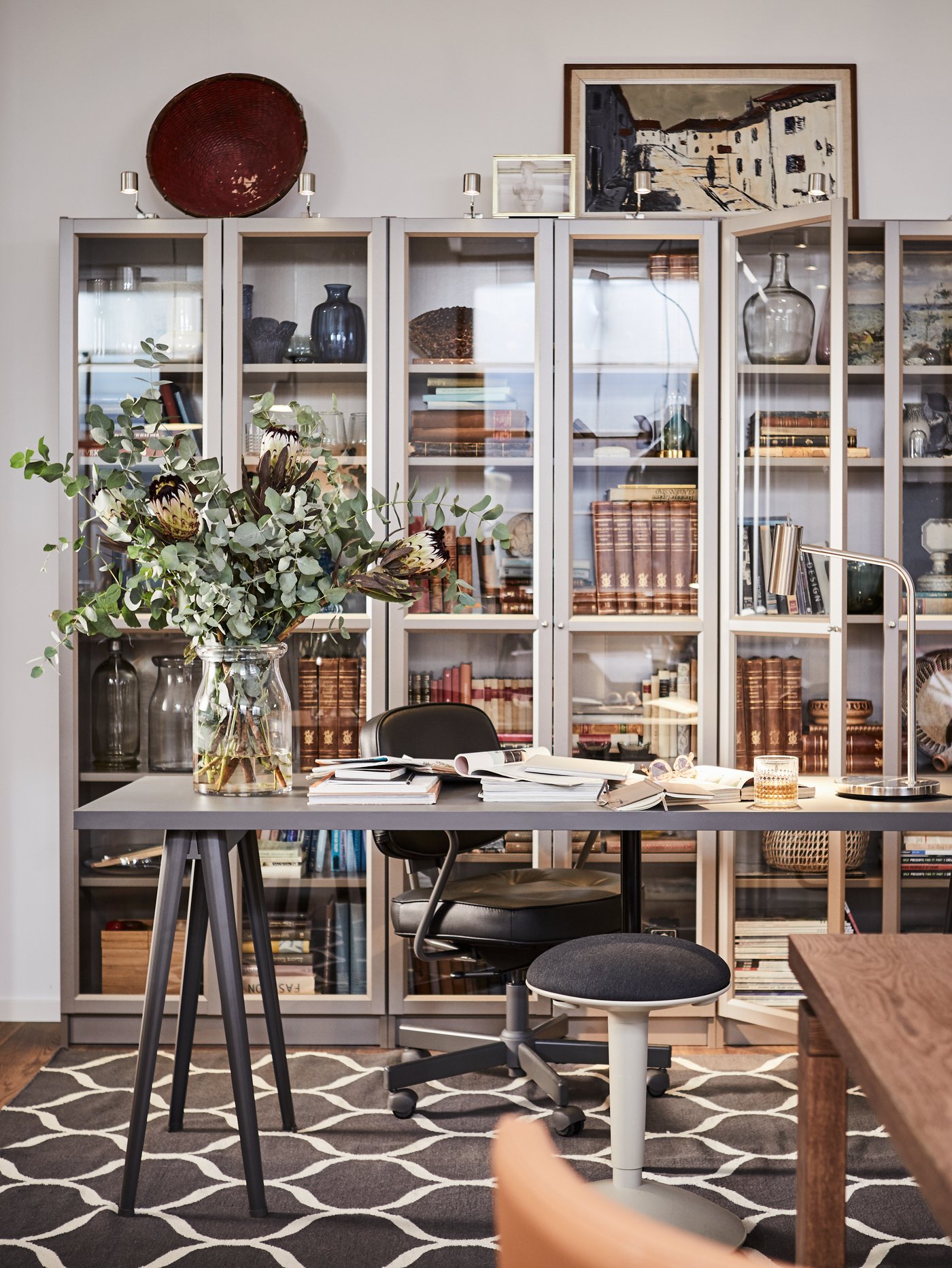A NÄRSPEL desk with flowers in a vase and documents on top and three BILLY bookcases behind filled with books and mementos.