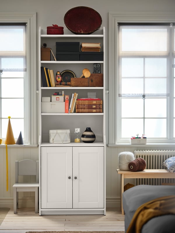 A light living-room corner with a grey HAUGA two-door high cabinet holding books, tableware and decorations.