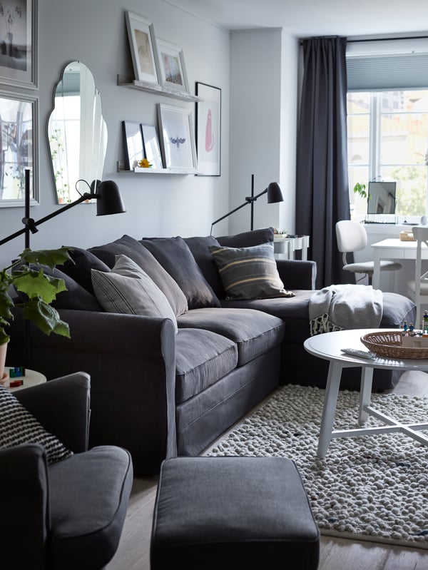 A grey GRÖNLID 3-seat sofa bed with chaise longue in a living room with a round white coffee table in front of it on a rug.