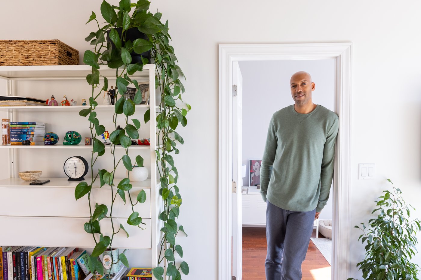 Man standing in clean white doorway, next to a bookcase with a plant hanging down.