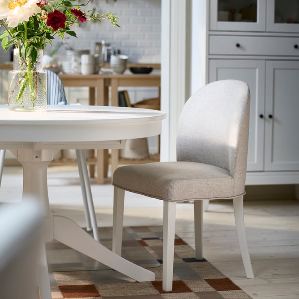 A fully-upholstered ROSENTORP chair in Kilanda light beige/white is placed next to a white ROSENTORP extendable table.
