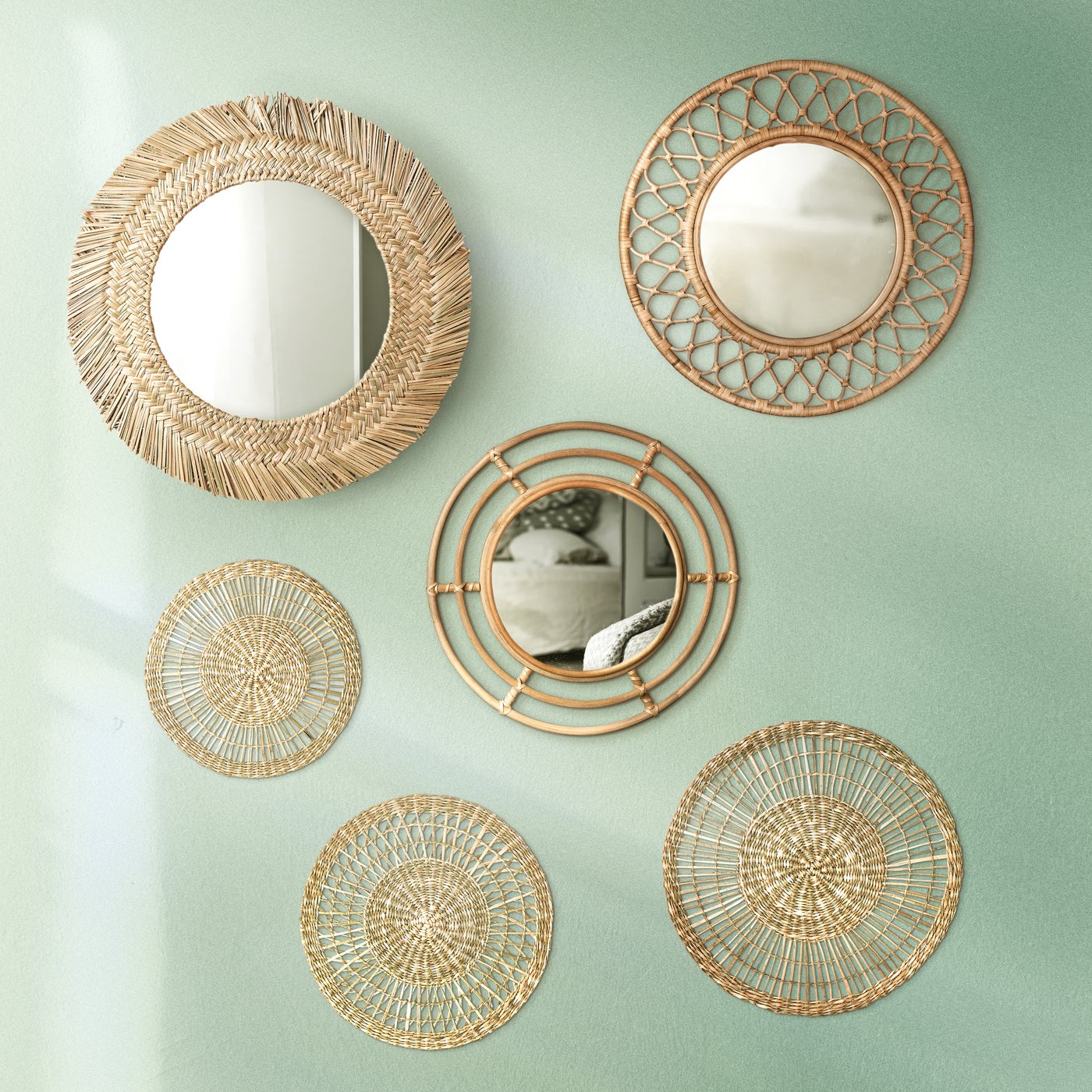 A collection of rattan BUSKBO mirrors hang on a light green wall.