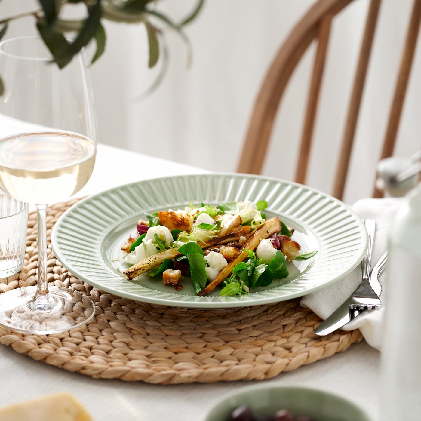 A STIMMIG plate and a wine glass on a table mat on a dining table.