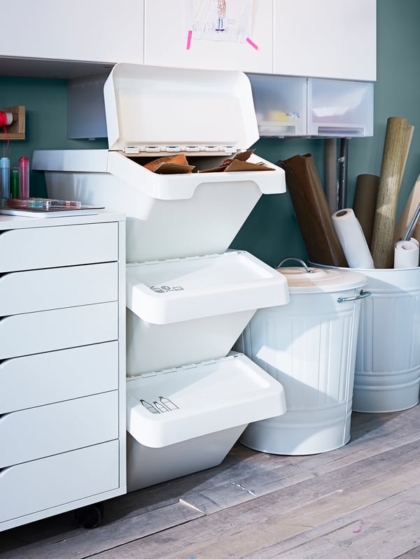 Three white SORTERA waste sorting bins with lid placed on top of each other, with the top bin open and filled with paper.