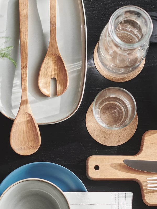 A black table set in geometric fashion with GLADELIG tableware and a knife and fork on a PROPPMÄTT beech chopping board.