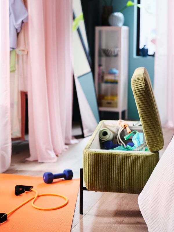 Banquette avec rangement VALTORP verte ouverte, dans laquelle est rangé du matériel de sport. Devant elle sur le sol, tapis de yoga et autres accessoires de sport.