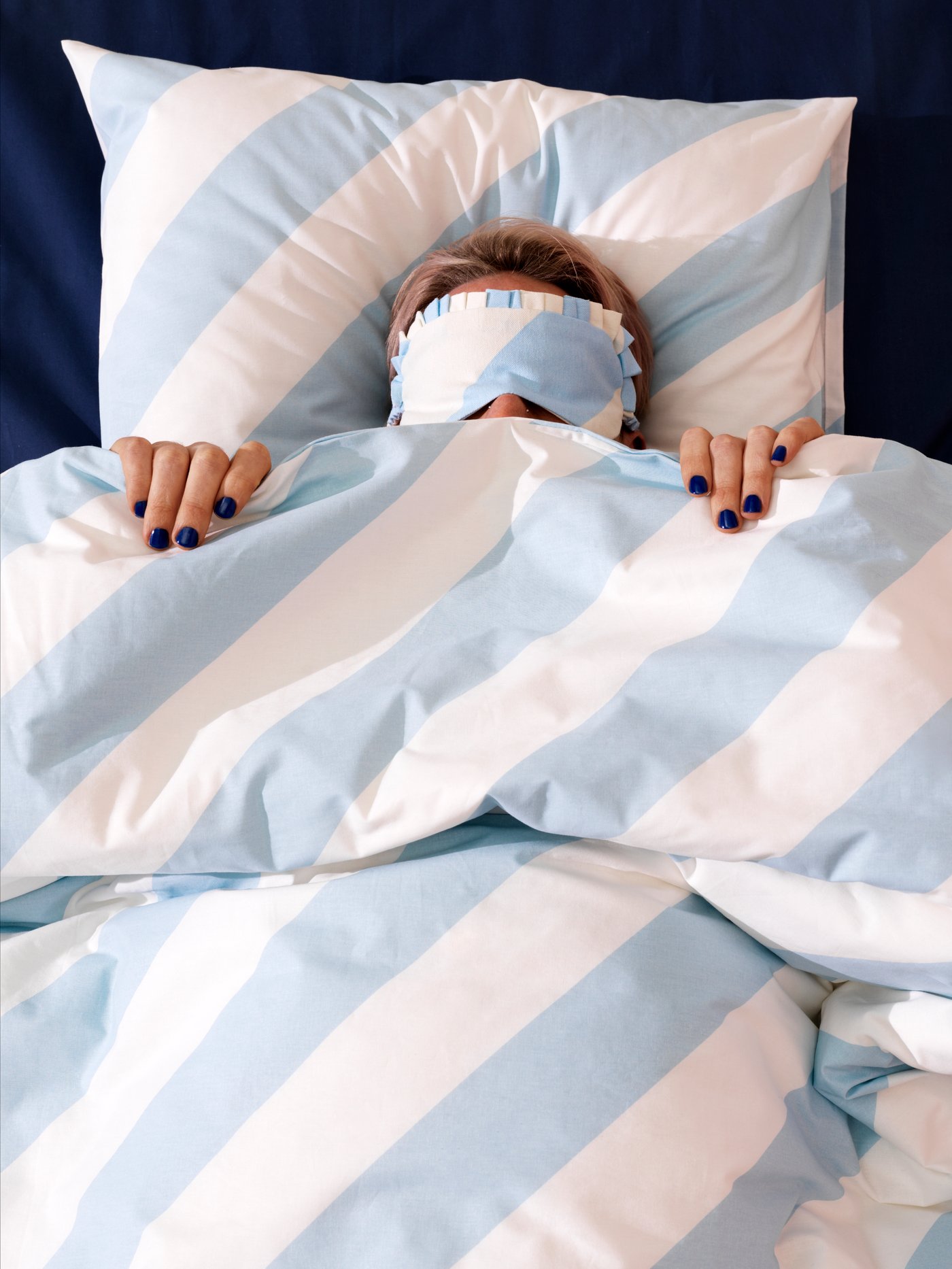 une personne portant un masque oculaire, allongée dans un lit, qui tire une couette vers son visage