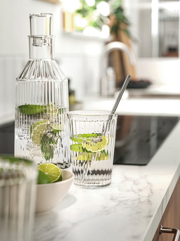 Una botella y un vaso llenos de agua y rodajas de limón sobre una cubierta EKBACKEN con un vivo efecto/laminado mármol blanco.