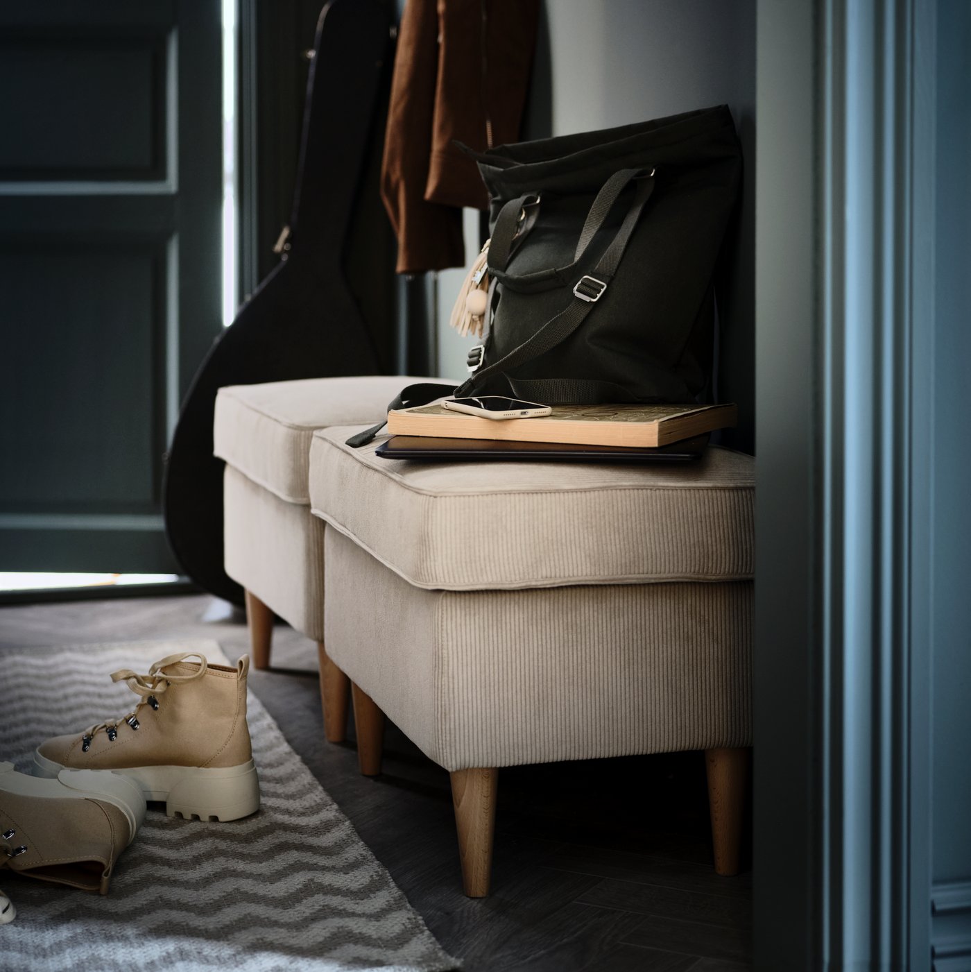 Two beige STRANDMON footstools line a hallway. Beneath them lie a pair of boots on a beige zigzag-patterned BREDEVAD rug.
