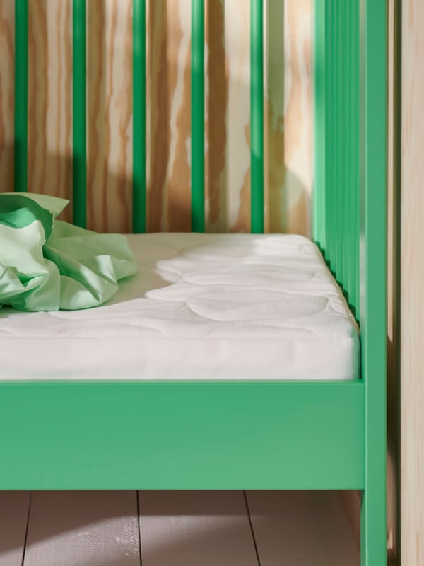 Extrémité d’un lit bébé GULLIVER vert dont un côté a été retiré, avec un matelas SKÖNAST et un drap vert froissé.