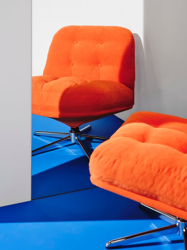 An orange DYVLINGE swivel armchair is placed on blue flooring in front of a mirror. The armchair is reflected in the mirror.