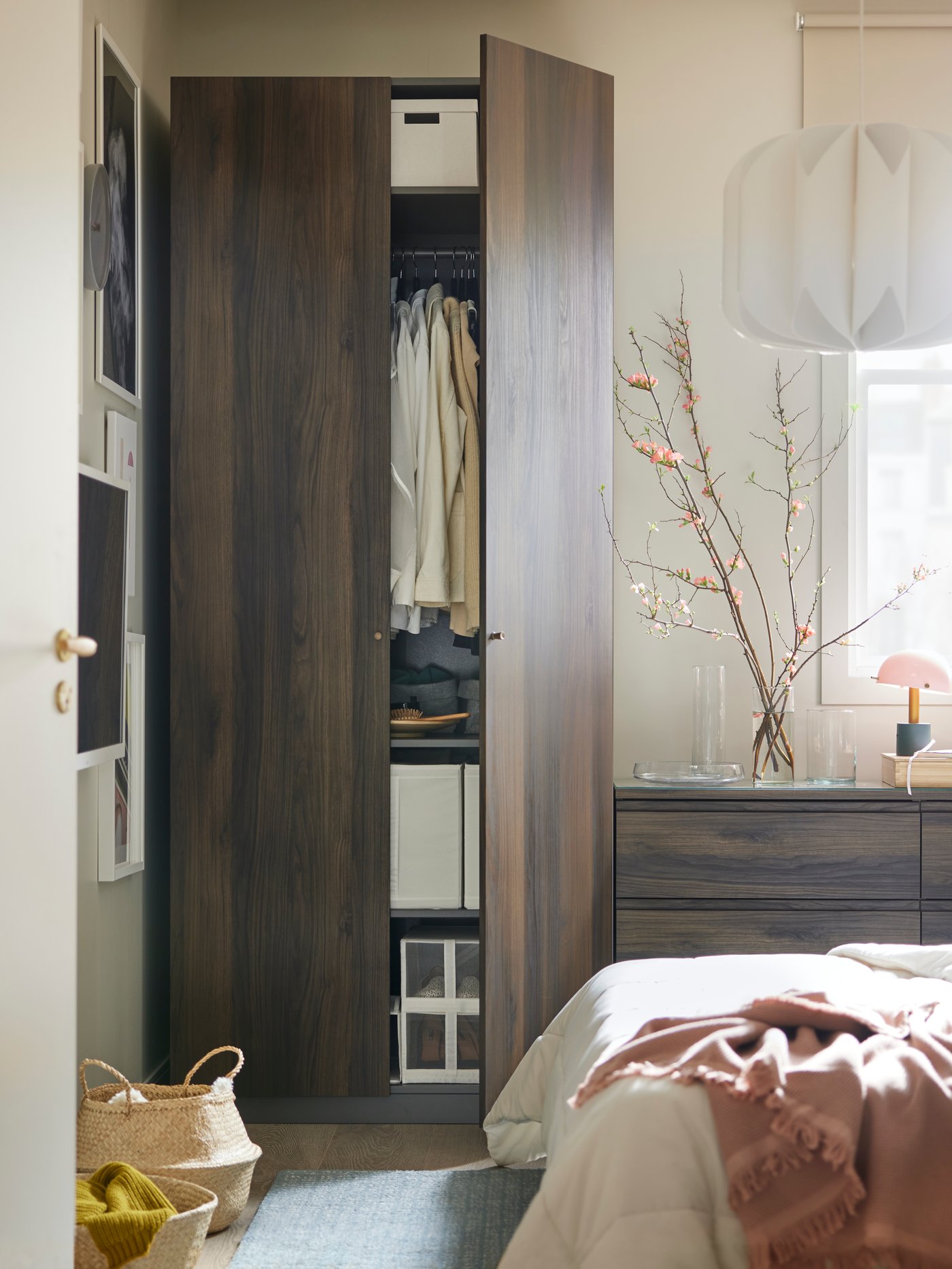 A PAX/STORKLINTA wardrobe beside a STORKLINTA chest with 3 drawers that has several glass vases and a table lamp on top.