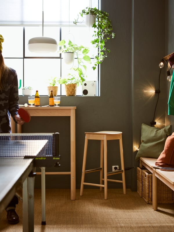 A room where a person plays table tennis next to a RÖNNINGE birch bar table and bar stool combination beneath a big window.