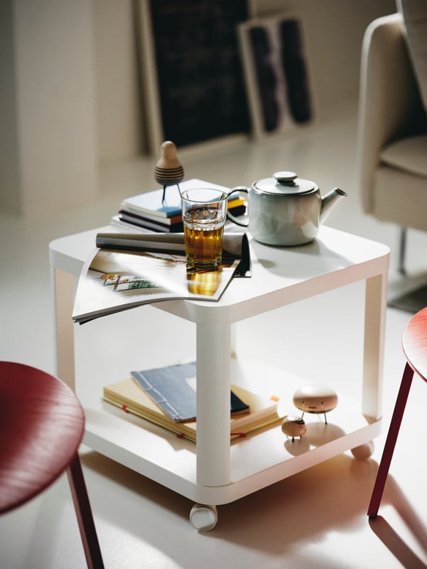 Magazines, books, a glass and a teapot on a white TINGBY side table on castors.