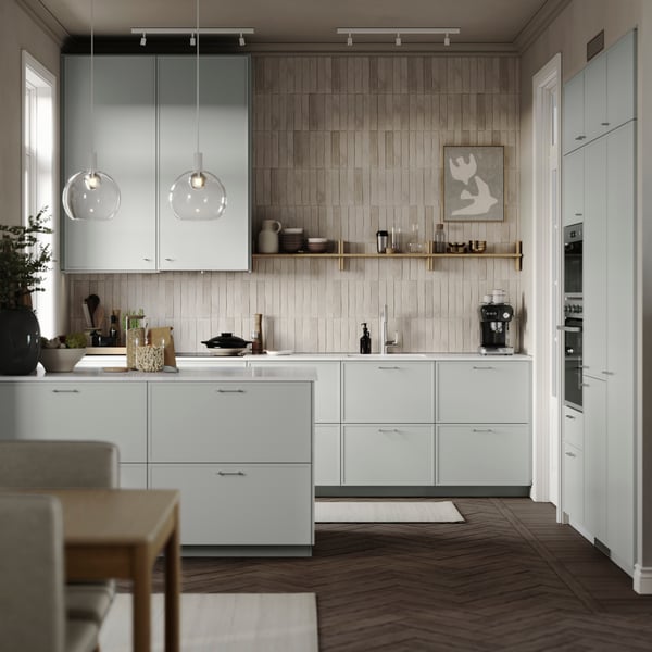 A contemporary kitchen with tiled walls, light-grey ASPUDDEN kitchen fronts, wooden floors, and a white worktop.