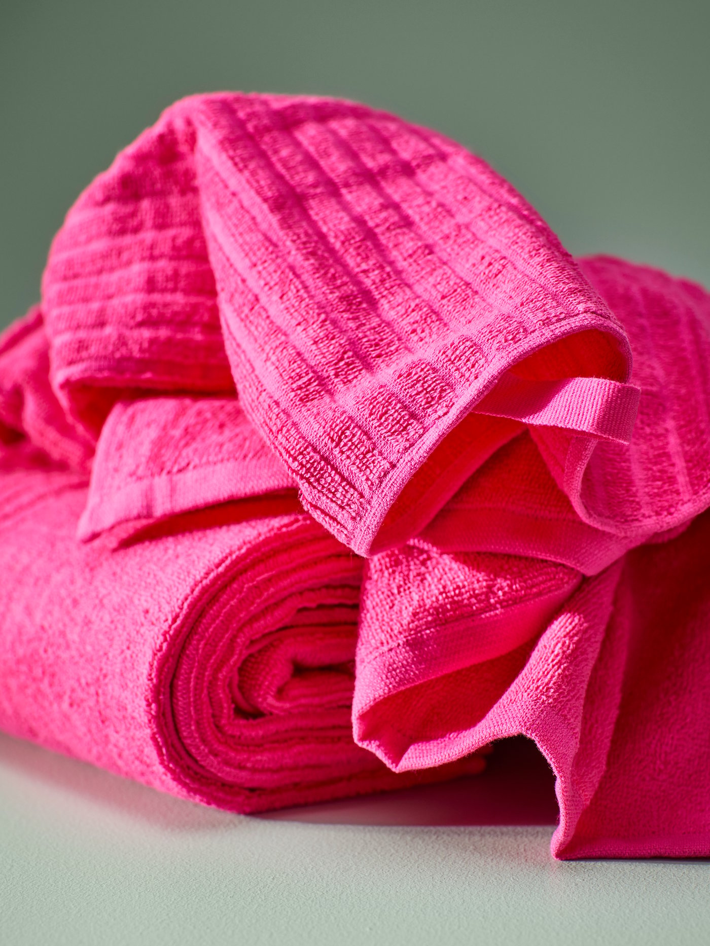 A bright pink VÅGSJÖN hand towel is roughly placed over a neatly folded VÅGSJÖN bath towel in bright pink.