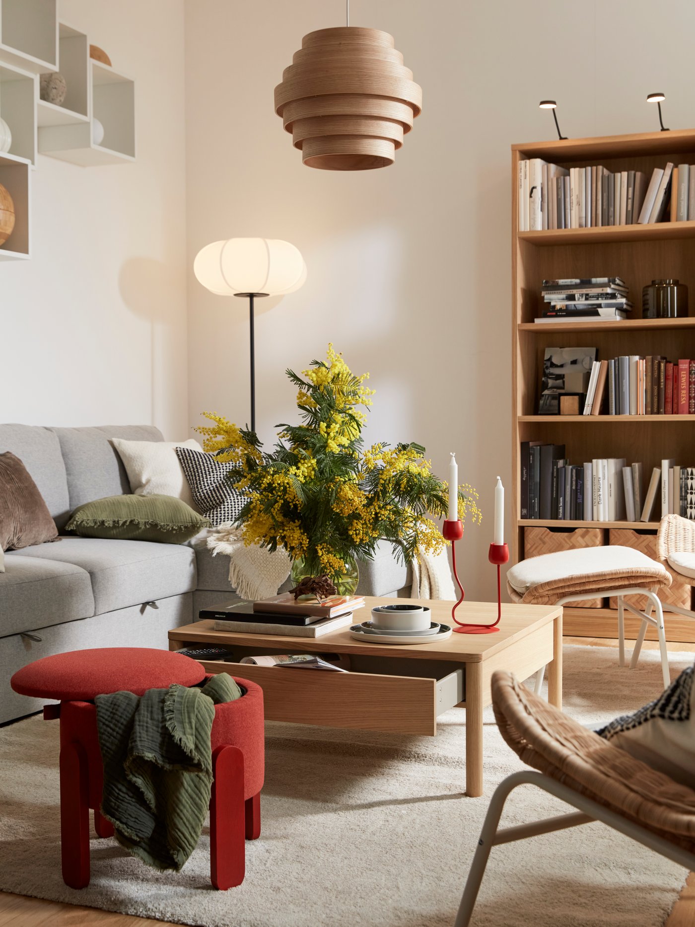 A light living room with a TONSTAD oak-veneer coffee table flanked by a BÅRSLÖV sofa-bed, a red pouffe and a STOENSE rug.