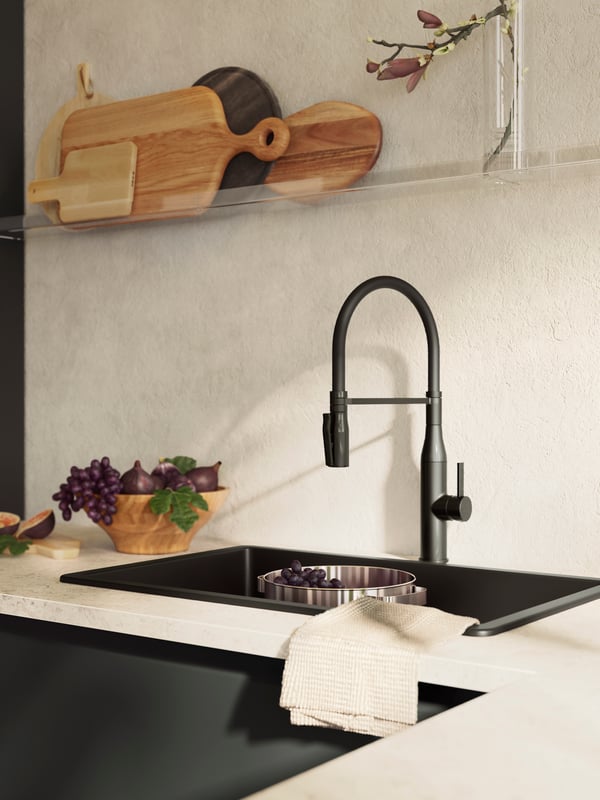 A sink with a TOLLSJÖN mixer tap in black polished metal, and a MELLÖSA picture ledge holding various chopping boards.