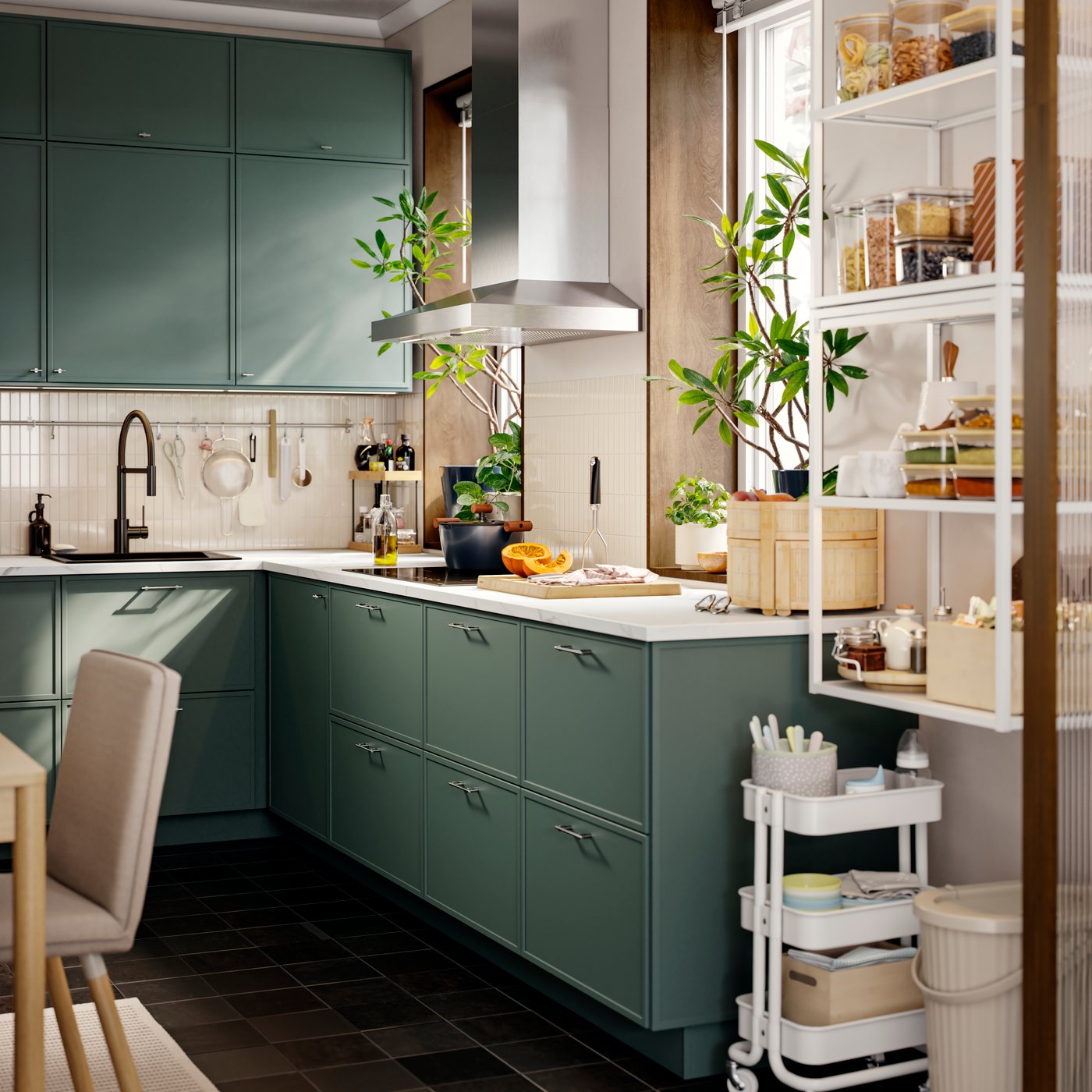 Una cocina pequeña con varios muebles bajos y gabinetes de pared con frentes ASPUDDEN en tono verde grisáceo, y una campana extractora ubicada junto a una ventana.