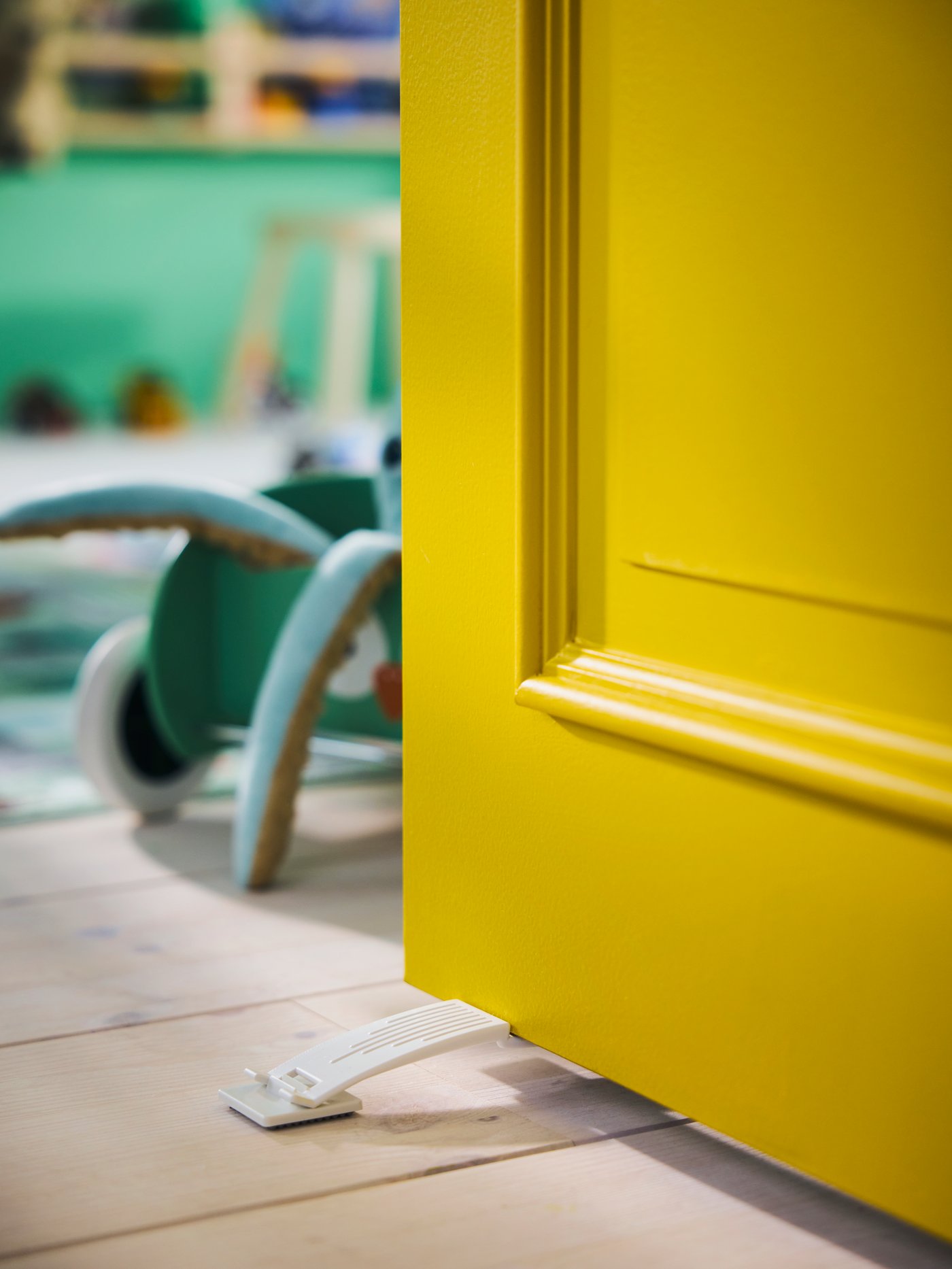 Close-up of a wooden floor and a bright yellow door stuck in open position thanks to PATRULL door stop.