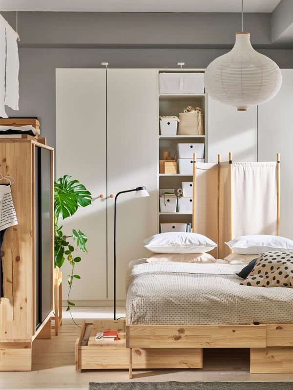 Bedroom in beige colours with GLAMBERGET bed, wardrobe and room divider in natural wood. White wardrobe in back.