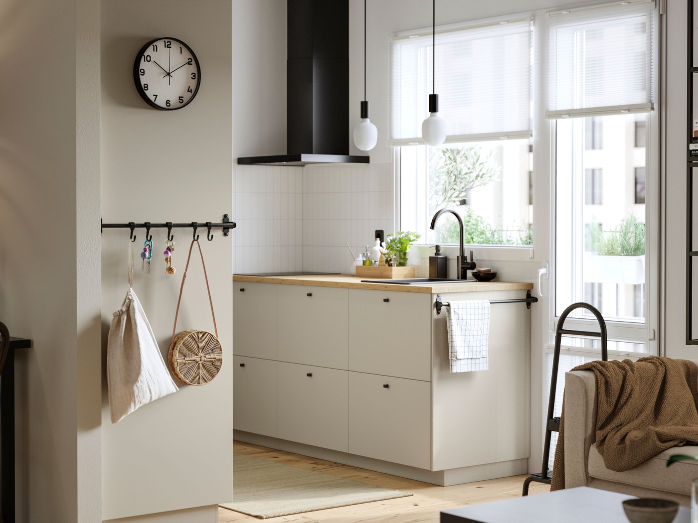 Eine Küche mit Fenster und Balkontür. Die Schränke sind mit beigefarbenen HAVSTORP Fronten versehen, an der Wand hängt eine MATÄLSKARE Dunstabzugshaube in Schwarz.