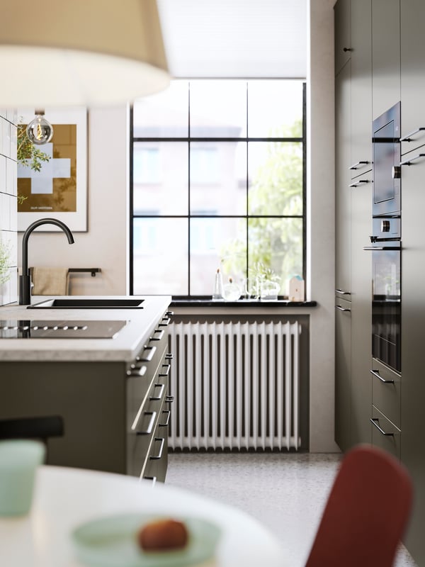 Et åbent køkken med brun-beige HAVSTORP køkkenfronter, sorte greb og hvidevarer samt en bordplade med kalkstensmønster.