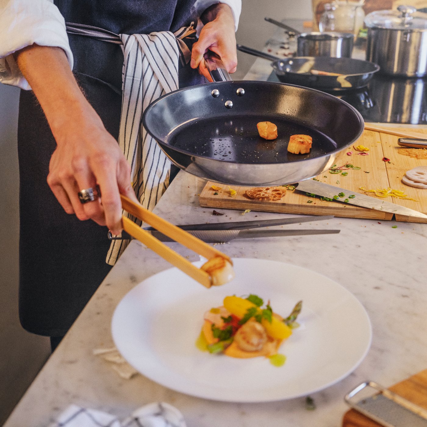 A person holds a 28 cm IKEA 365+ frying pan with nonstick coating while using wooden tongs to remove and plate prepared food.