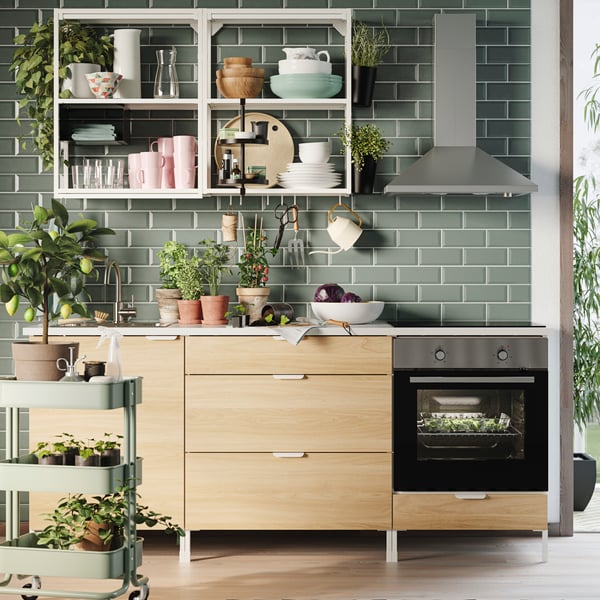 A green, tiled kitchen wall with white/oak effect ENHET cabinets and drawers below the worktop and white wall shelving.