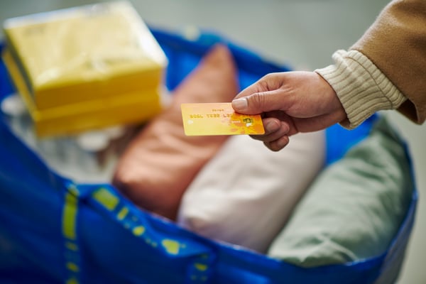 Osoba drži karticu za plaćanje iznad kese FRAKTA pune IKEA proizvoda.