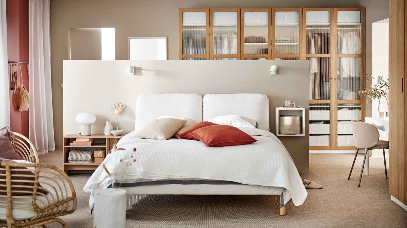 A large, light Japandi style bedroom with a white SAGESUND upholstered bed in the middle covered in white bed linen.